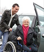 caregiver helping woman in a wheelchair get into a car