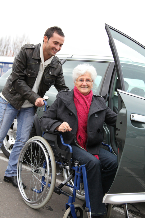caregiver helping woman in a wheelchair get into a car