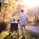 man walking with a woman in a wheelchair along a path in autumn